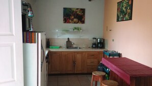 A compact kitchen with wooden cabinets, a white refrigerator, and a red countertop. There are two stools and a small sink. - Pink house (San Antonio Palopo)