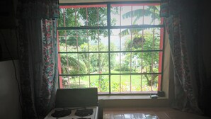 A kitchen with a gas stove, a window with a view of greenery, and curtains. - Pink house (San Antonio Palopo)
