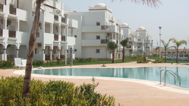 Un complexe hôtelier comprenant plusieurs bâtiments blancs, une piscine et des palmiers.