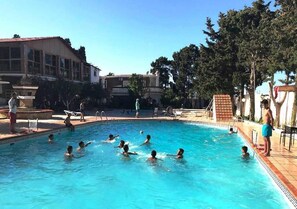 Une piscine où l’on voit des personnes dans l’eau, entourée d’immeubles et d’arbres.