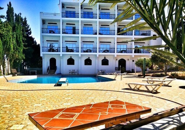 Un hôtel à plusieurs étages doté d’une piscine, d’un espace extérieur aménagé et d’une terrasse carrelée.