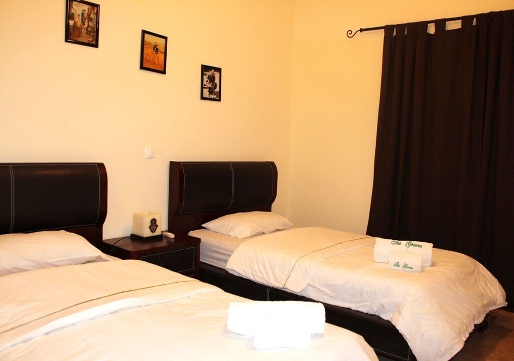 A hotel room with two single beds, a nightstand with a phone, and a curtain on the window.