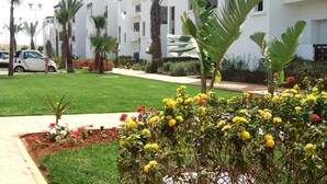 A residential building with multiple balconies, a well-maintained lawn, and a variety of flowering plants. - The Greens Residence 3621 (SAIDIA)