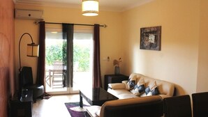 Een woonkamer met een bank, een salontafel, een lamp, een stoel en een schuifdeur die leidt naar een buitenruimte.