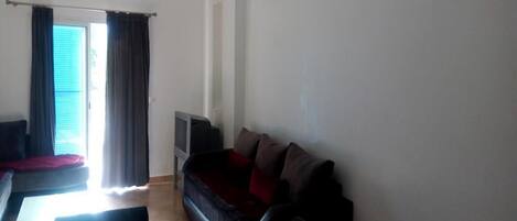 A living room with a sofa, a TV, a coffee table, and a window with curtains.