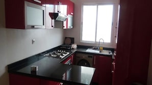 Una cocina con gabinetes rojos, una encimera negra, estufa, fregadero y ventana.