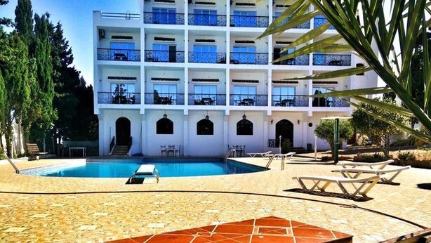 Un hôtel à plusieurs étages doté d’une piscine, d’un espace extérieur aménagé et d’une terrasse carrelée.