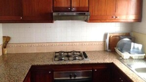 A kitchen with wooden cabinets, a gas stove, and a dishwasher. - Java Rasmile Residence 2906 (Mdiq)