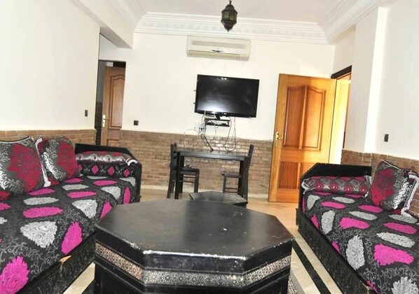 A living room with a sofa set, a coffee table, and a TV mounted on the wall. - Residence Barrone Marrakech 3377 (Marrakech)