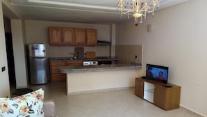 A living room with a sofa, a television, and a kitchen area with wooden cabinets and a refrigerator. - Atlantic Ocean Residence 3044 (Asilah)