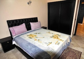 A bedroom with a bed, two nightstands, a black wardrobe, and a patterned bedspread.