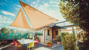 A patio with a table and chairs, a large shade sail, and potted plants. - A Casa B&B (Ravenna)