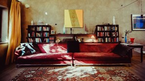 A cozy living room with a red sofa, two bookshelves, a patterned rug, and a painting on the wall. - A Casa B&B (Ravenna)