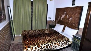 Une chambre à coucher avec un lit, des rideaux verts, une tête de lit à motifs et une table de chevet.