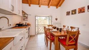 Una cocina con armarios blancos, techo de madera y un comedor con sillas y mesa de madera.