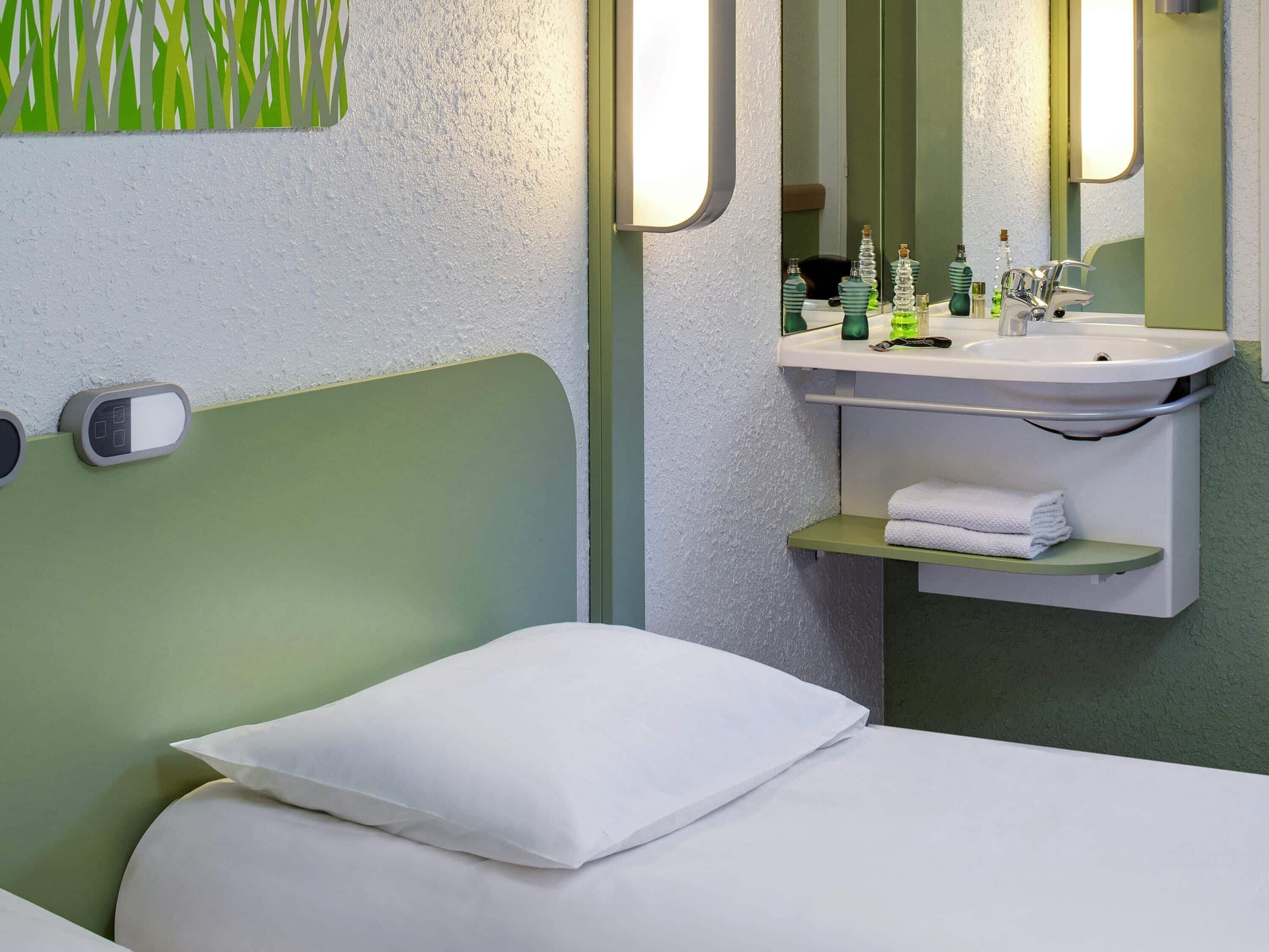 Hotellihuone, jossa on sänky, yöpöytä, peili, pesuallas ja pyyheteline.