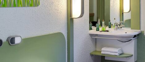 Habitación de hotel con cama, mesita de noche, espejo, lavamanos y perchero para toallas.