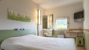 Une chambre d’hôtel avec un lit, un petit bureau, un miroir, une télévision et une fenêtre.