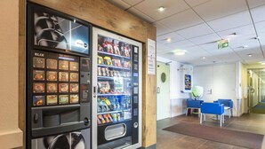 Un distributeur automatique proposant diverses boissons, un espace d’accueil avec un comptoir et des chaises, et un couloir menant à d’autres pièces.