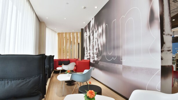 Un hall d’hôtel moderne doté d’un espace détente avec des canapés gris, une table blanche agrémentée d’un vase de fleurs et une grande œuvre d’art abstraite murale.