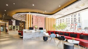 Un espace d’accueil moderne avec un comptoir incurvé, un coin salon avec des canapés rouges et une grande fenêtre donnant sur la rue.
