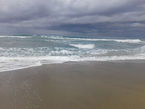 Une plage où les vagues se brisent sur le rivage sous un ciel nuageux.