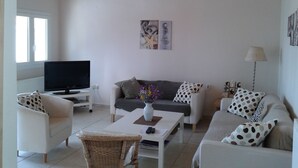 Een woonkamer met een televisie, twee banken, een salontafel en een rieten fauteuil.