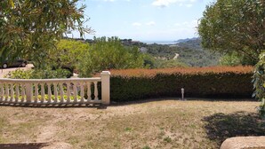 A landscaped garden with a white fence, a hedge, and a view of a coastal landscape. - Mini-villa No. 4 - 2/4 people (PORTO-VECCHIO)