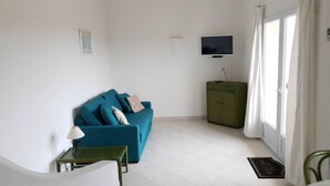 A living room with a teal sofa, a small table with a lamp, a green cabinet, and a TV on the wall. - Mini-villa No. 4 - 2/4 people (PORTO-VECCHIO)