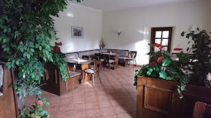 A dining area with a long table and chairs, surrounded by potted plants and a framed photo on the wall. - Gaststätte und Pension Erbgericht (Großhartmannsdorf)