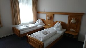 Two wooden beds with white linens and pillows, a wooden nightstand, a wooden headboard, a window with curtains, and a wall-mounted light fixture. - Gaststätte und Pension Erbgericht (Großhartmannsdorf)