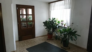 A room with a wooden door, a window with lace curtains, and several potted plants. - Gaststätte und Pension Erbgericht (Großhartmannsdorf)