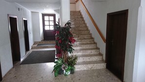 A hallway with a staircase, a potted plant, and a door at the end. - Gaststätte und Pension Erbgericht (Großhartmannsdorf)