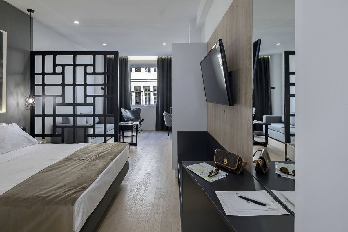 A modern hotel room with a bed, desk, and seating area.