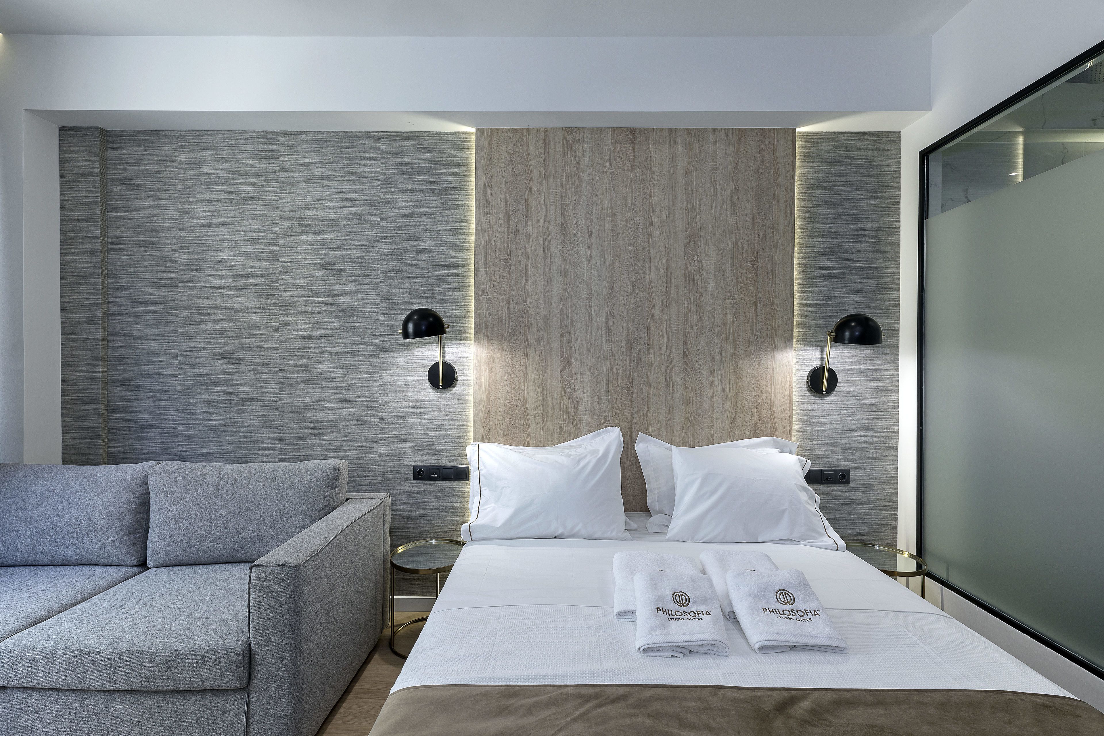 A modern hotel room with a bed, a grey sofa, and a small side table.