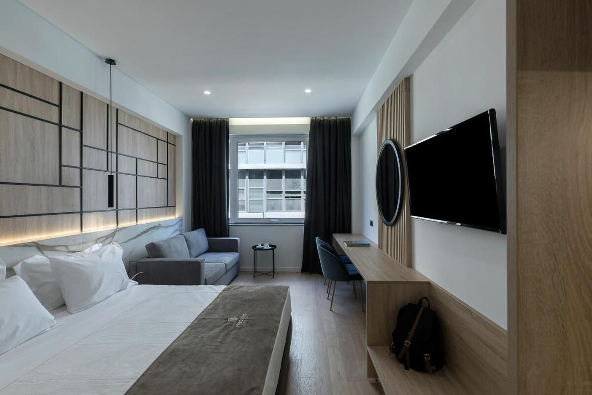 Ein modernes Hotelzimmer mit einem Bett, einem Schreibtisch, einem Fernseher und einem fensterbelaubten Fenster.