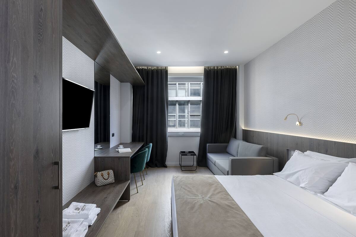 A modern hotel room with a bed, a desk, a chair, a sofa, and a TV.