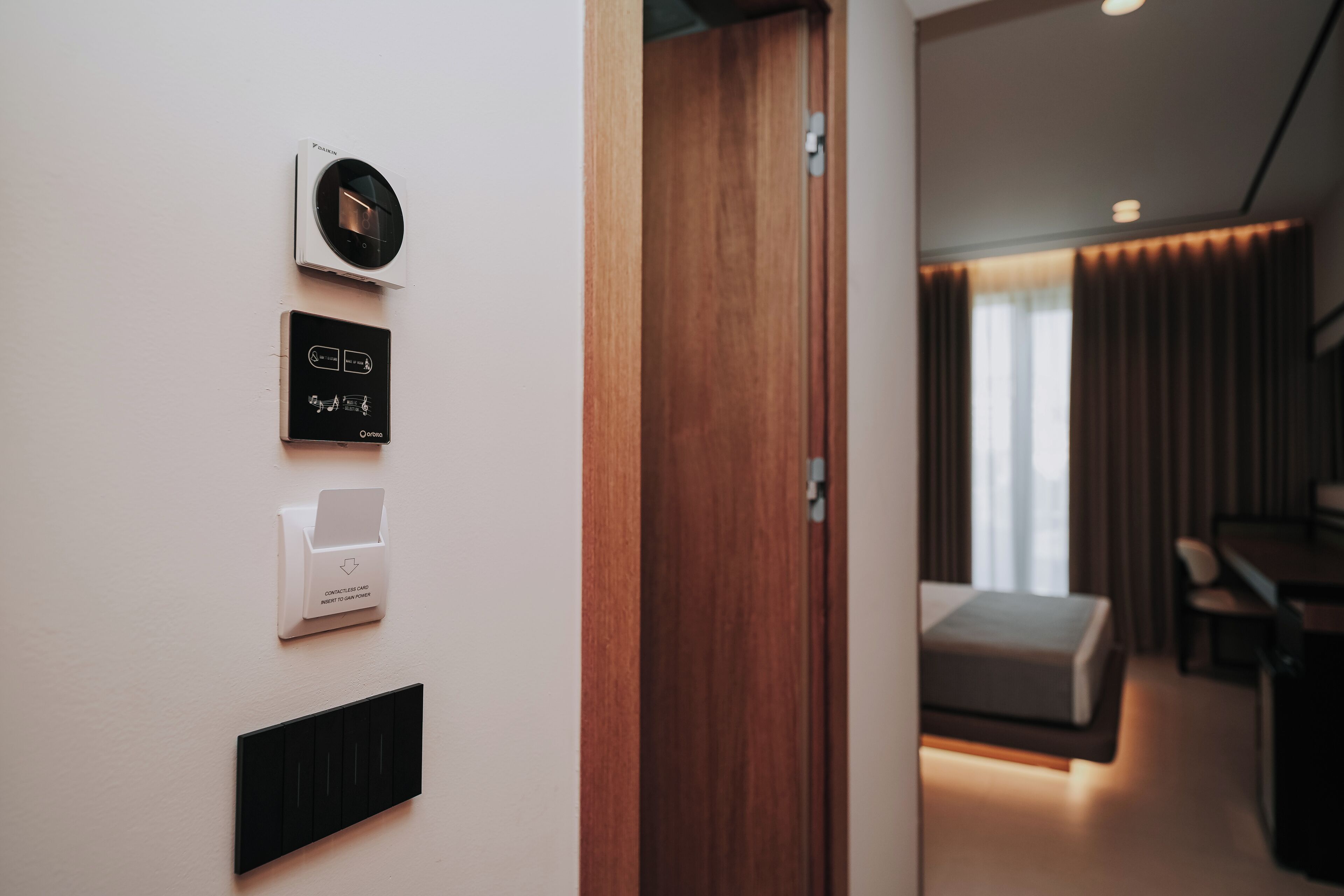 A modern hotel room with a wall-mounted air conditioning unit, a contactless card reader, and a control panel with music and light settings.
