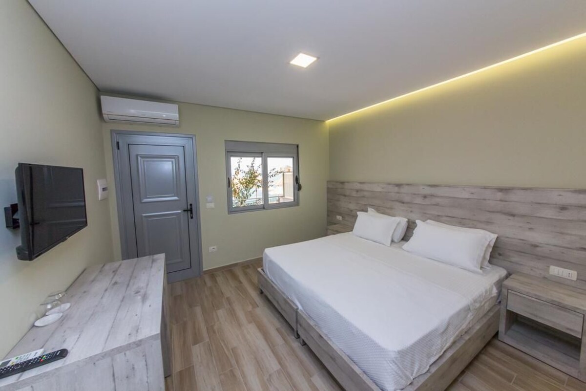 Un dormitorio con cama, televisión montada en la pared, una puerta y una ventana.