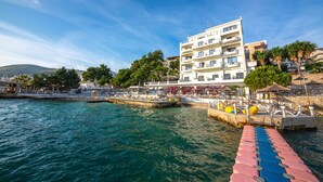 A waterfront hotel with multiple balconies, a pier with lounge chairs, and a view of the sea. - Hotel Jaroal (Sarandë)