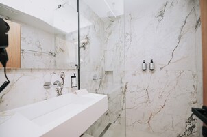A modern bathroom with a white marble sink, a glass shower enclosure, and a mirror with a wooden panel.