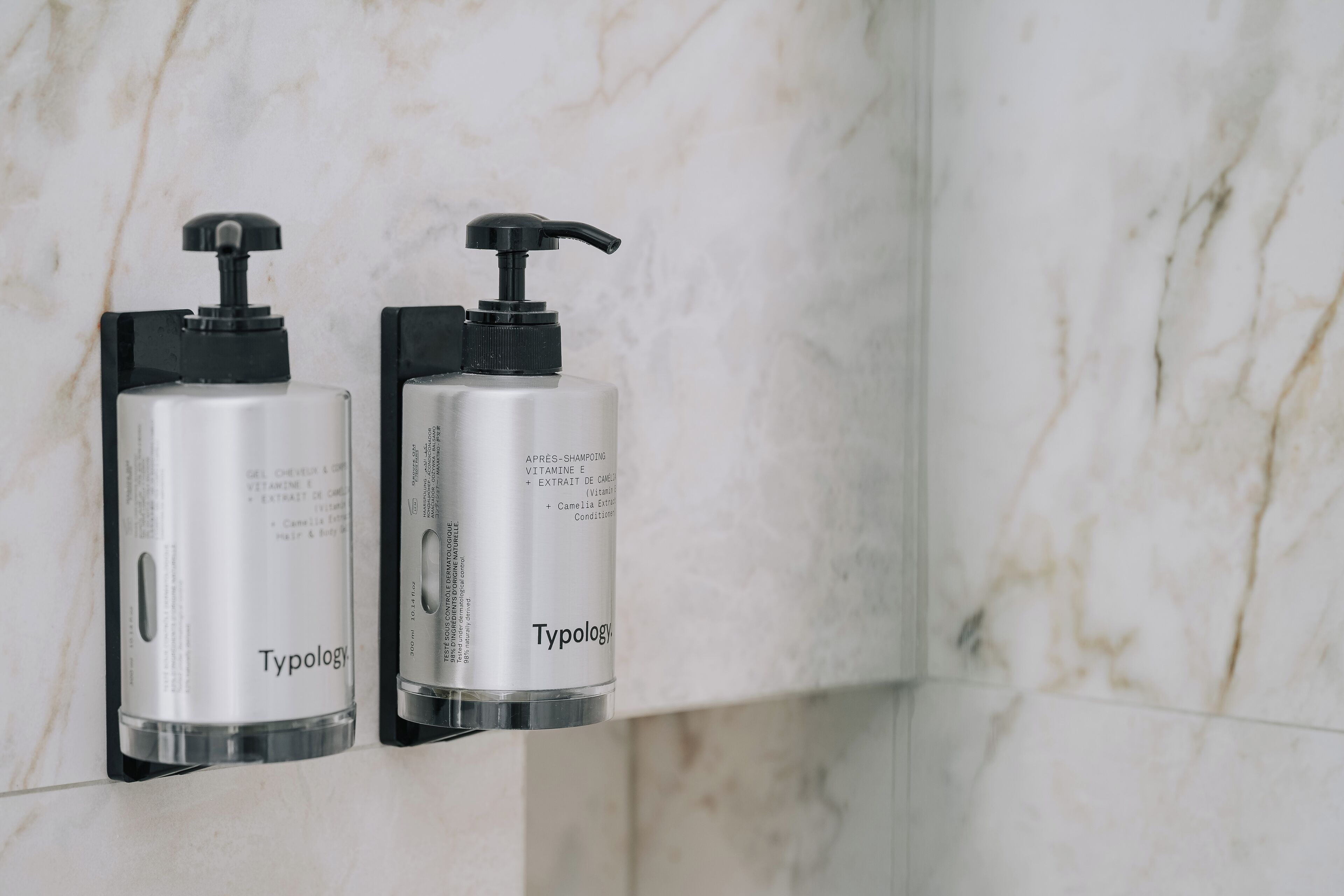 Two Typology branded dispensers mounted on a marble wall.