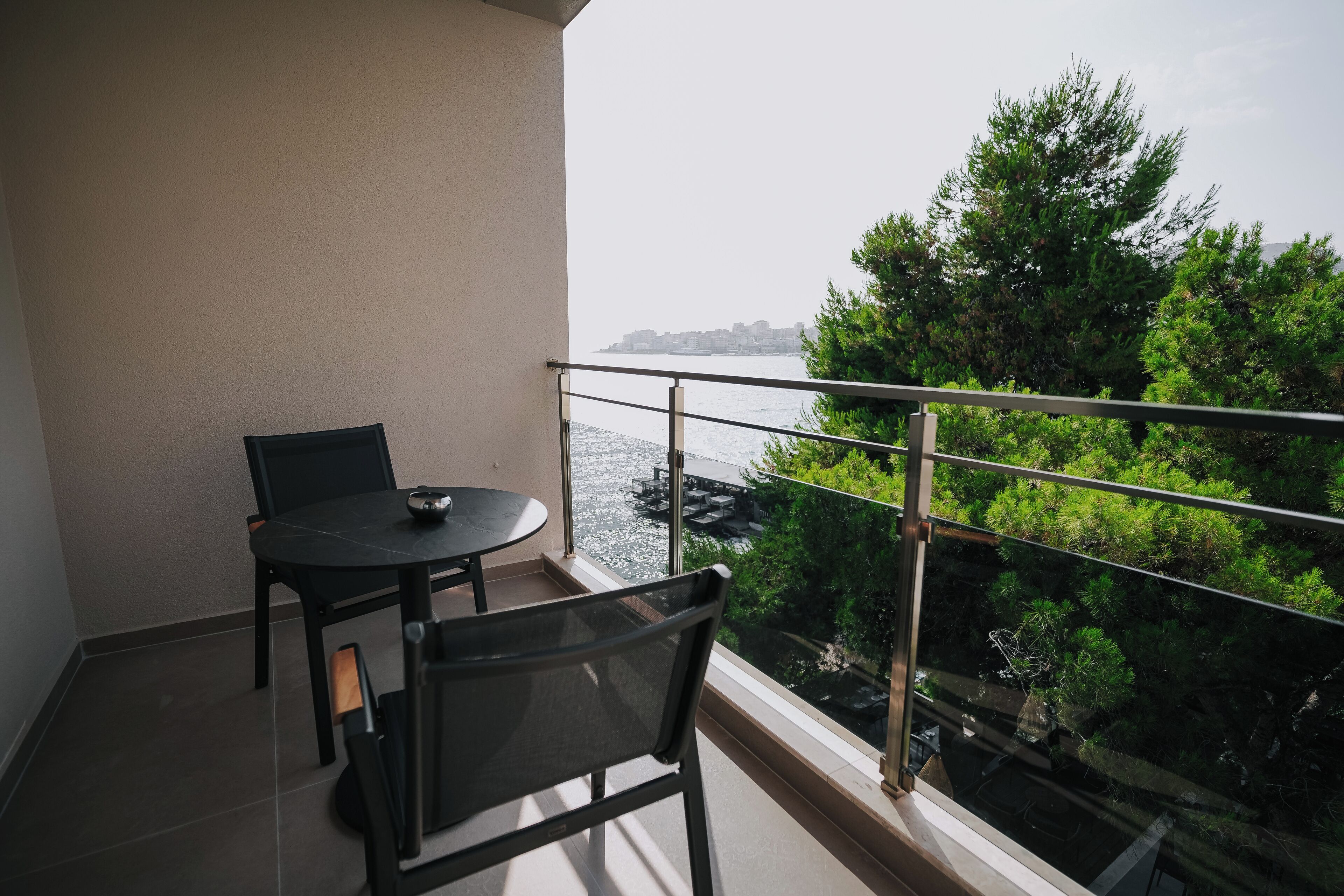 A balcony with a table and chairs, overlooking a body of water and greenery.