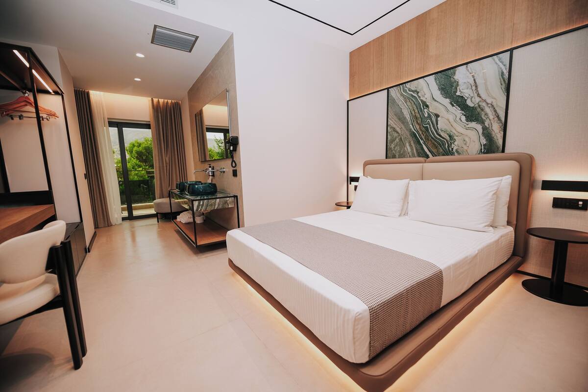 A modern hotel room with a large bed, a desk, and a view of the outdoors.