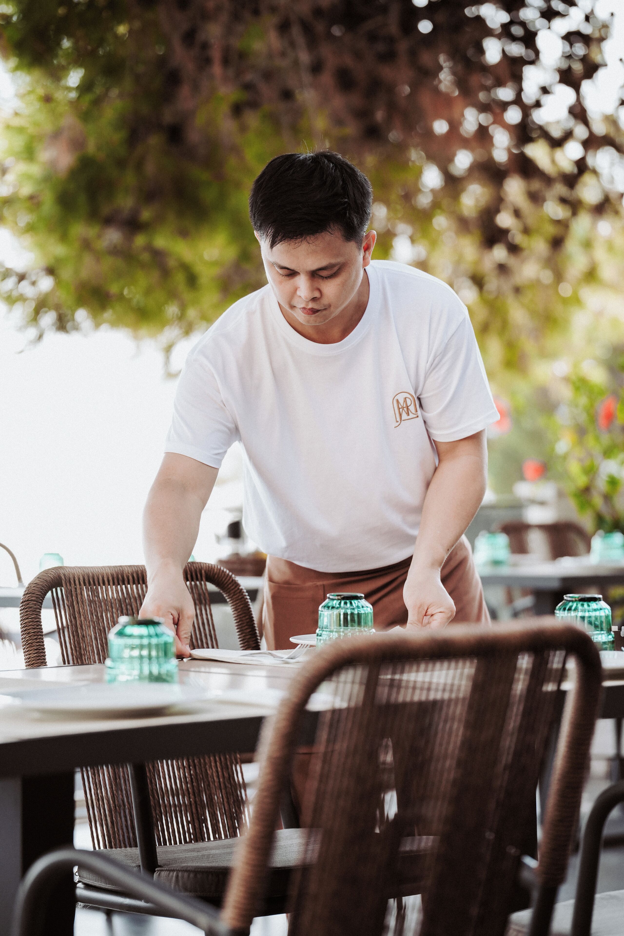 Une personne dispose des objets sur une table dans un cadre extérieur, avec des chaises en osier et une table à manger.