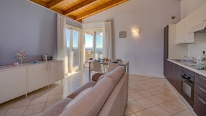 A modern living room with a wooden ceiling, a sofa, a dining area with a table and chairs, and a kitchen with cabinets and a sink. - Fedra (Manerba del Garda)