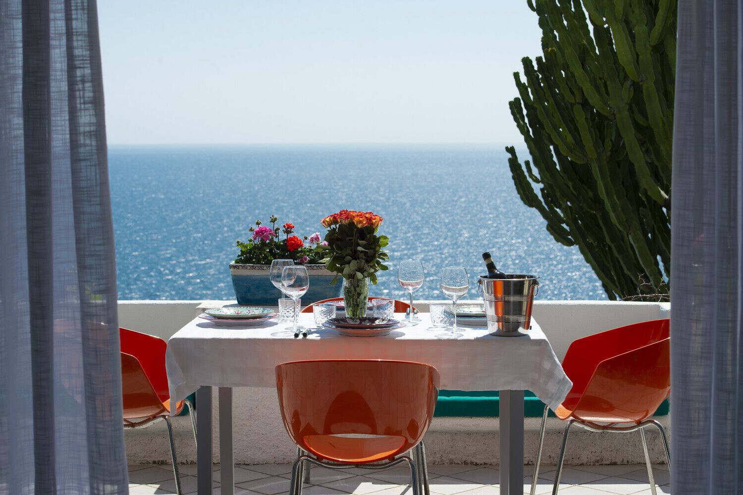 Une table dressée pour deux personnes, avec vue sur la mer, agrémentée d’une plante en pot et d’une bouteille de champagne.