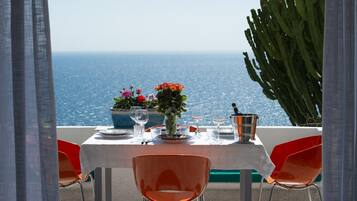 Une table dressée pour deux personnes, avec vue sur la mer, agrémentée d’une plante en pot et d’une bouteille de champagne.