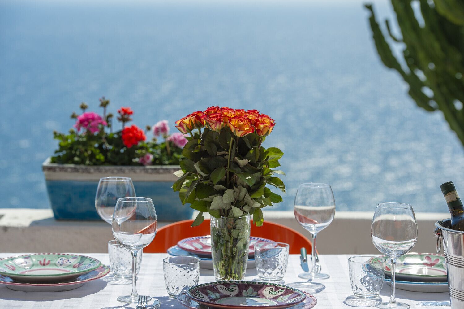 Ein Esstisch mit Meerblick, eine Blumenvase und eine Weinflasche.