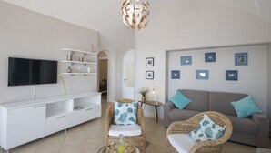 A modern living room with a flat-screen TV, white console, wicker chairs, a grey sofa, and wall-mounted picture frames. - Casa Giovannina - charming fisherman's house with stunning views (Conca dei Marini)